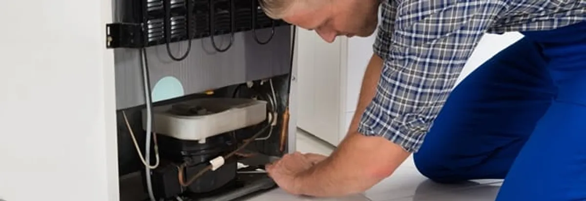 Refrigerator repair technician servicing the compressor and condenser area in Toledo, OH